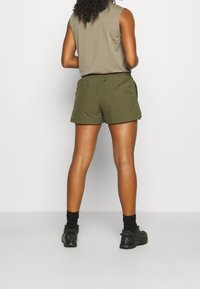 Shorts verts avec une coupe décontractée, fabriqués dans un tissu léger, dotés de poches latérales et de détails à la taille, associés à des baskets noires.