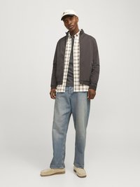 Dark gray bomber jacket, white checkered shirt over gray top, light blue loose jeans, and beige moccasin shoes; cream cap with logo.