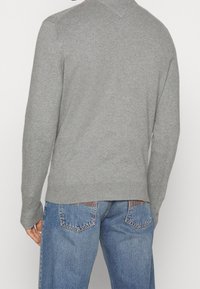 Maglione grigio lavorato a maglia con scollo rotondo, polsini e orlo a coste, abbinato a jeans di denim blu con tasche posteriori dettagliate con cuciture.