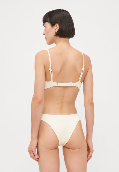 Haut de bikini crème à côtes avec bretelles réglables et fermeture à crochet, associé à un bas de bikini taille basse assorti. Texture lisse, design minimal.