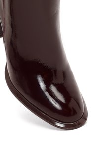 Stivale alla caviglia in pelle bordeaux con finitura lucida, punta affusolata e design senza cuciture. Estetica minimalista con una texture liscia.