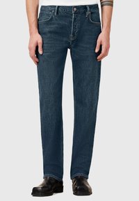 Jeans de mezclilla azul oscuro con un diseño de pierna recta, que cuentan con bolsillos frontales, un cierre de botón y acentos de costura visibles.