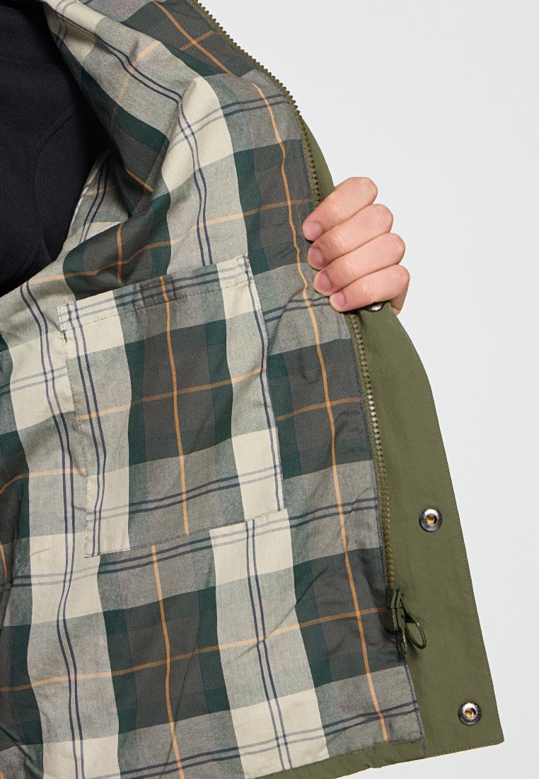 Olijfgroene jas interieur met een groen, beige en oranje ruitpatroon. Beschikt over twee binnenzakken en metalen drukknopen.