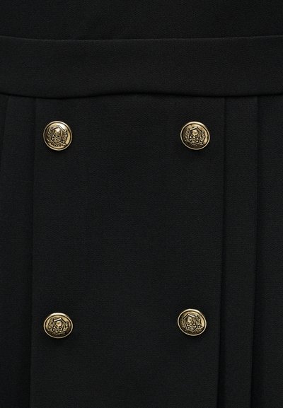 Μαύρο ύφασμα με τέσσερα χρυσά κουμπιά τοποθετημένα ομοιόμορφα, καθένα με έμβλημα κρανίου και λουλουδιού σε εξαγωνικό πλαίσιο.