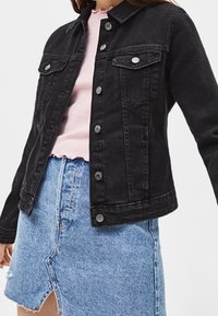 Svart jeansjacka med krage, framfickor och silverknappar, kombinerad med en rosa ribbad topp och en blå jeanskjol med slits fram.