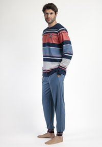 Camisa de pijama de manga larga a rayas en navy, rojo y gris con un logo; combinada con pantalones de color azul claro con tobillos acampanados y acentos rojos.