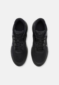 Baskets de sport noires avec un dessus en maille texturée, un logo Nike en gris contrastant et une semelle extérieure en caoutchouc arrondie. Comprend un système de fermeture à lacets.