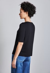 Haut noir à manches courtes avec un col rond, associé à un jean bleu taille haute. Le tissu semble lisse avec une coupe décontractée.