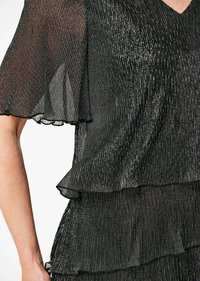 Robe noire avec une texture plissée scintillante ; présente des volants superposés aux manches et à l'ourlet, un tissu léger et fluide, ainsi qu'un décolleté en V.