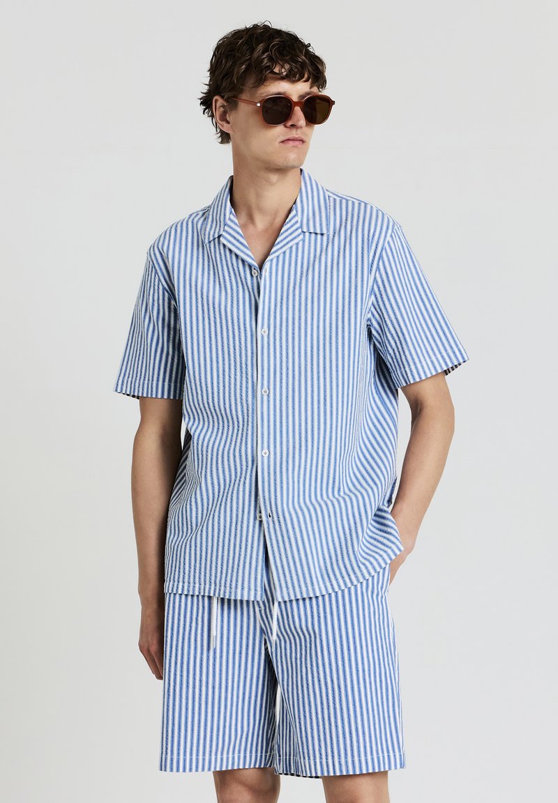 Gestreiftes blau-weißes Kurzarmhemd und passende Shorts aus leichtem Stoff mit Knopfverschluss und frontalen Taschen.