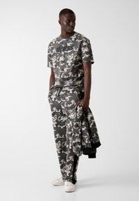 Tuta mimetica in tonalità di grigio e nero, composta da una maglia a maniche corte e pantaloni con coulisse, realizzata in tessuto morbido con finitura testurizzata.