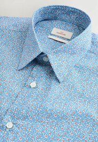 Blå skjorta med mönster och blommotiv bestående av små orange och gröna motiv. Har krage med knappar och vita knappar.