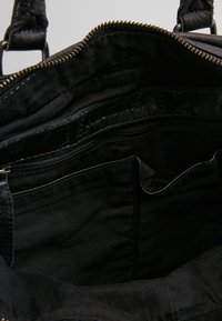 Intérieur de sac à main noir avec une doublure texturée, plusieurs compartiments, y compris une poche zippée, et une finition en tissu lisse.