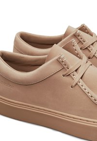 Sneaker in pelle color beige chiaro con texture liscia, design minimalista, dettagli cuciti e lacci. Logo visibile sul lato.