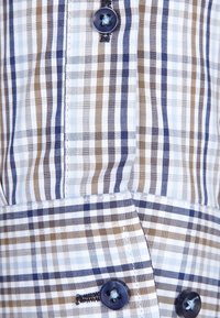 Košile na knoflíky s modrým, hnědým a bílým kostkovaným vzorem. Vyrobená z lehké látky s tmavě modrými knoflíky a kontrastním šitím.