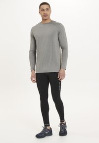 Grijs langarm sportshirt met een ronde hals, gecombineerd met zwarte leggings met de tekst "Elite Lab" en zwarte hardloopschoenen.