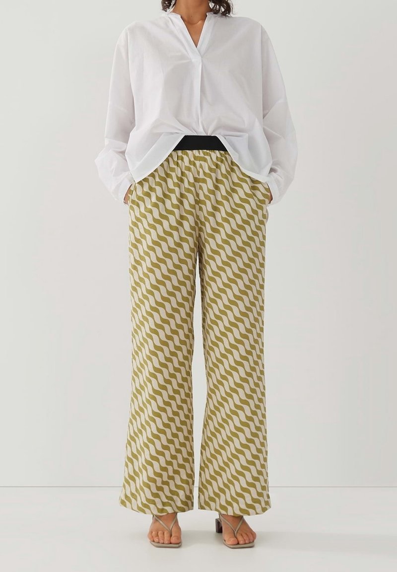 Vit långärmad skjorta i kombination med olivgröna och gräddfärgade mönstrade vida byxor med en vågig design och en elastisk svart midja.