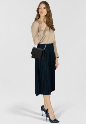 Schwarze Leder-Umhängetasche mit Kettenriemen, beigefarbene Bluse mit V-Ausschnitt, dunkler plissierter Rock und marineblaue spitze High Heels.