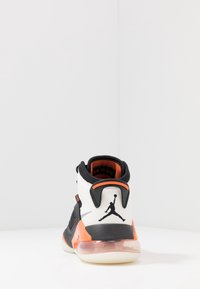 Tenisky Air Jordan s bílým koženým svrškem, černými akcenty, oranžovými detaily, síťovanými panely a průhlednou vzduchovou mezipodešví. Obsahuje logo na patě.