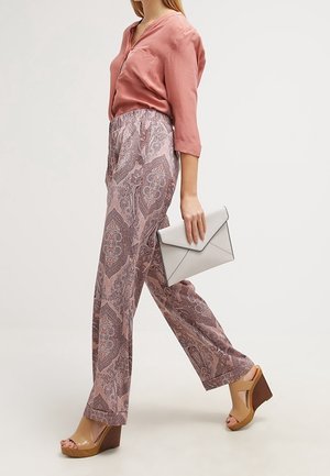 Blusa de seda rosa claro con cuello en V, combinada con pantalones anchos estampados en rosa y gris. Acentuada con cuñas beige y un bolso de mano gris.