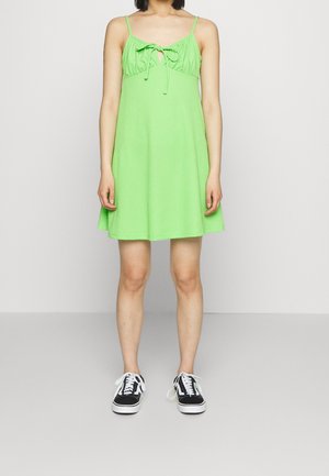 Robe A-line vert clair avec un corsage froncé, des attaches réglables au niveau du cou et des bretelles spaghetti, associée à des baskets noires.