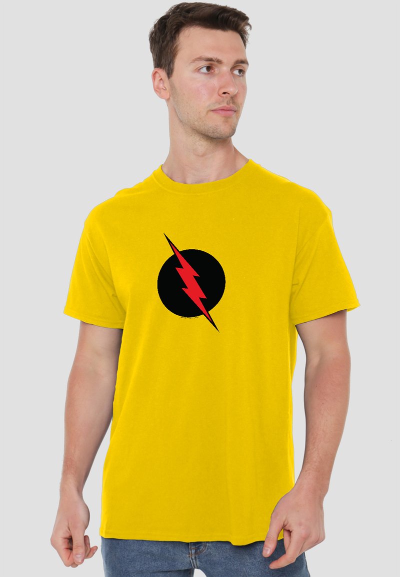 Man wearing a bright yellow t-shirt with a black circle and red lightning bolt design, looking to his right against a light background.