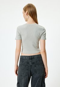 Vaaleanharmaa ribattua pinta-alaa omaava lyhythihainen crop-top, yhdistettynä tummanharmaisiin korkeavyötäröisiin reisitaskuhousuihin, joissa on kaksi takataskua.