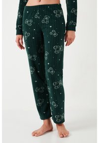 Pantaloni de pijama verde închis, cu dungi, cu modele albe de ursuleț și stele, purtați desculți cu bluză cu mânecă lungă asortată.
