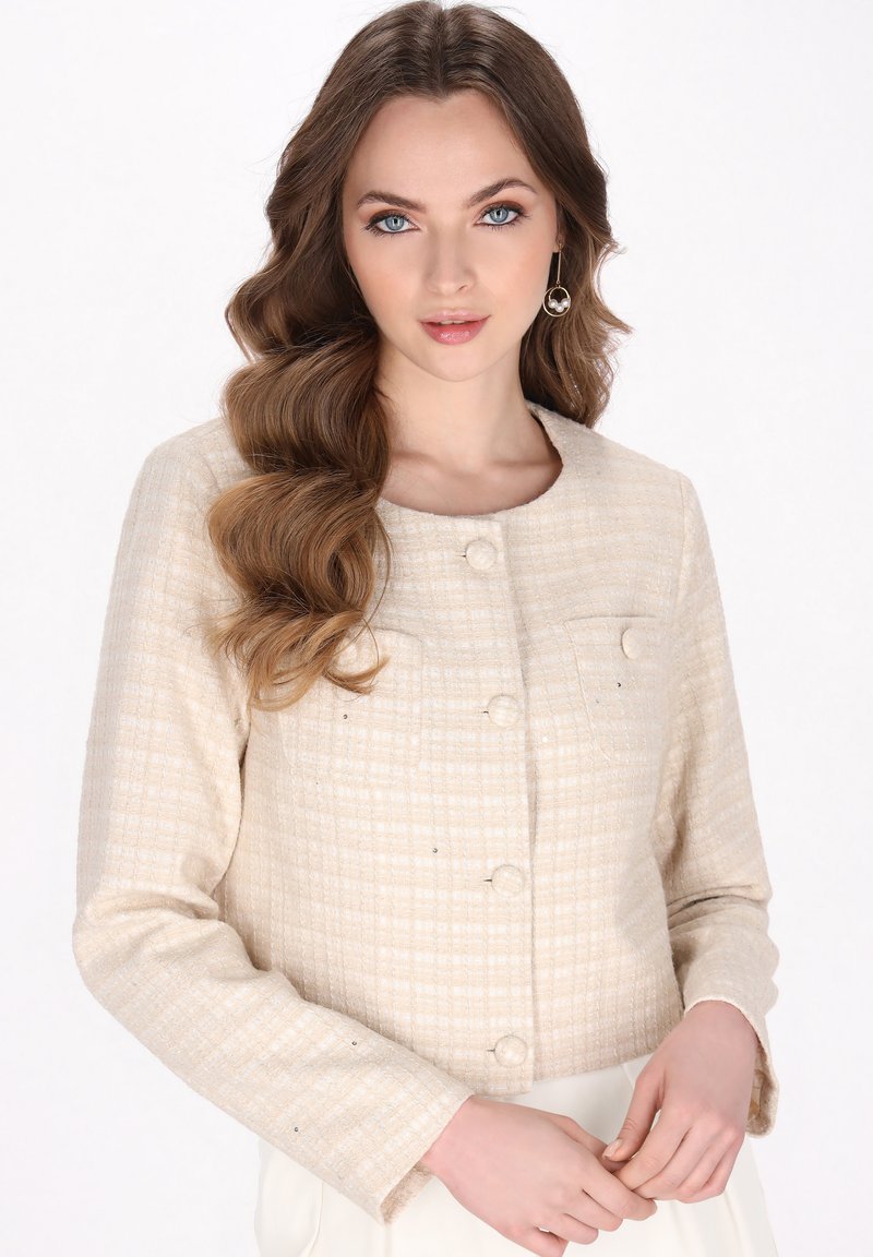 Giacca beige, in tessuto a trama, con motivo a scacchi, caratterizzata da maniche lunghe, bottoni frontali e dettagli con due tasche.