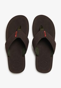 Chanclas marrones con una suela beige, que presentan una tira de goma en verde oscuro, detalles de costura y un logo de la marca en la plantilla.