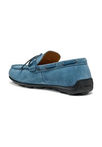 Zapato de barco azul de ante con suela de goma negra, con diseño de cordones y ojales plateados. Textura suave con punta ligeramente redondeada.