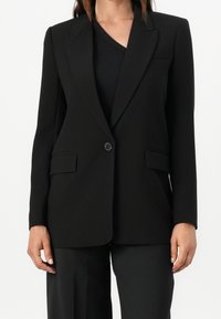 Musta bleiseri räätälöidyssä muotoilussa, jossa on yksittäinen nappikiinnitys, kaksi etutaskua ja sileä kangasrakennetta.