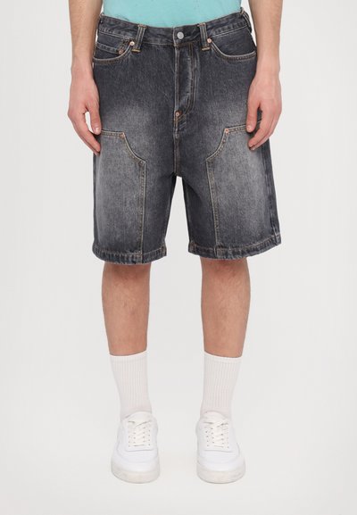 Pantaloni corti in denim scuro con una vestibilità rilassata, dotati di cinque tasche, cuciture a contrasto e orlo arrotolato. Abbinati a sneaker bianche e calze.