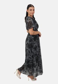 Maxi kjole i gennemsigtigt sort materiale med blomstermønster. Har korteærmer og elastisk talje. Blevet stylet med hvide strophæle.