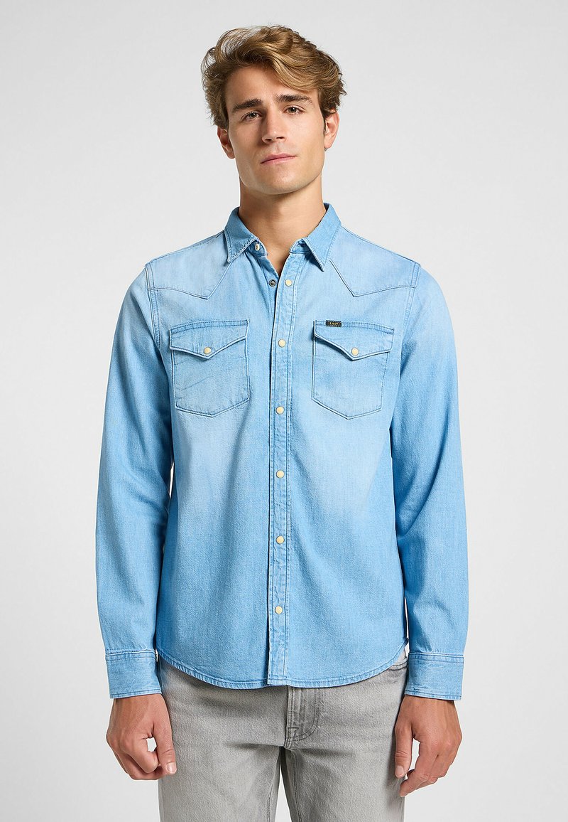 Camisa de mezclilla azul claro con un diseño clásico del oeste, que cuenta con dos bolsillos en el pecho, costuras de yugo puntiagudas y cierres de botones.