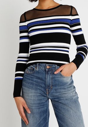 Zwart gestreepte lange mouwen top met blauwe, witte en zwarte horizontale lijnen; heeft een doorzichtige mesh halslijn en geribbelde textuur. Gecombineerd met blauwe jeans.
