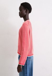 Langärmliges Shirt in Rot- und Weißstreifen mit Rundhals und geknöpften Ärmeln, kombiniert mit blauen Jeans.