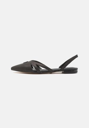 Sort spids tå flad slingback-sko med udskæringer på siderne og lav hæl på en ensfarvet hvid baggrund.