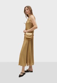 Zlaté maxi šaty bez rukávů s bočním rozparkem. V kombinaci se strukturovanou hnědou kabelkou přes rameno s řetízkovým popruhem a černými zdobenými balerínami.