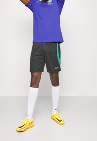 Sportovní oblečení Nike zahrnující fialové tričko, černé šortky se zelenými akcenty, bílé ponožky a jasně žluté boty s černými detaily.