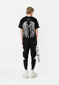 Camiseta gráfica negra con un gran diseño de alas blancas en la parte posterior, combinada con pantalones jogger negros y botas gruesas blancas.