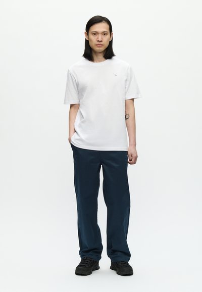 Camiseta blanca de algodón con un pequeño logo en el pecho, combinada con pantalones sueltos de color azul marino y zapatillas negras.