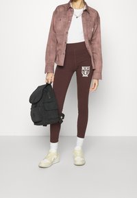 Hnědé legíny s bílým logem Nike, světle béžové tričko, mauve sukně koženková bunda a černý batoh. Bílé ponožky a světlé tenisky.