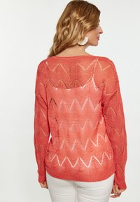 Korallfarbener Strickpullover mit Zickzackmuster, langen Ärmeln und geripptem Saum, mit offener Webstruktur und Rundhalsausschnitt.