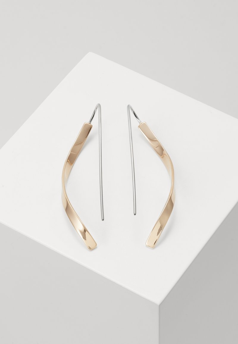 Zlate in srebrne viseče uhane z ukrivljeno, podolgasto obliko. Sijajna površina z gladko teksturo in minimalističnim oblikovanjem.