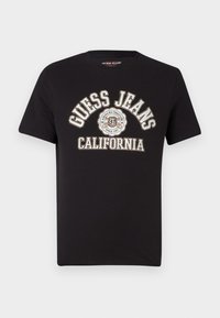 Camiseta de algodón negra con gráfico de "Guess Jeans California" en blanco y rojo, cuello redondo y mangas cortas con una textura suave.