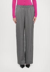 Svart og hvit mønstrete vide bukser med elastisk midjebånd, med et gjentakende bladdesign. Bær med en lys rosa cardigan.