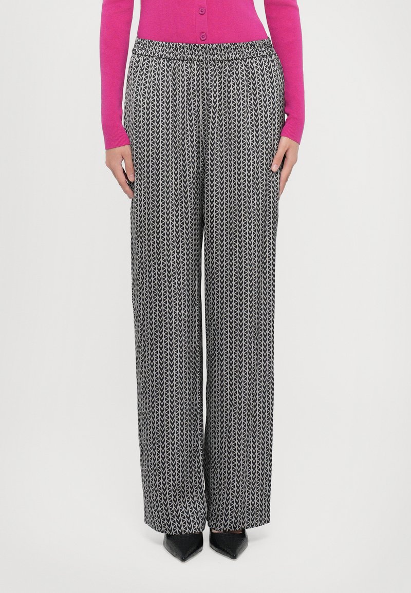 Svart og hvit mønstrete vide bukser med elastisk midjebånd, med et gjentakende bladdesign. Bær med en lys rosa cardigan.