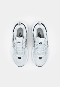 Valged ja mustad Nike tossud tekstuurse pealispinnaga, ümar kuju, silmatorkav nöörimise süsteem ja pehmendusega tald. Omab logo aktsente.