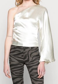 Top na jedno rameno ve lesklém slonovinovém saténu, zdobený detailním řasením a kalhotovým rukávem. V páru s olivově zelenými džínami s pruhy zebry.